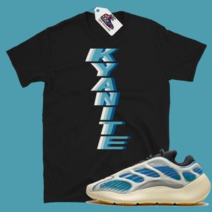 Może przedstawiać: Czarny T-shirt z nadrukiem słowa "KYANITE" w pionie, niebieskimi i białymi literami. Koszulka jest połączona z białymi i niebieskimi butami sportowymi z ż&oacute;łtą podeszwą.