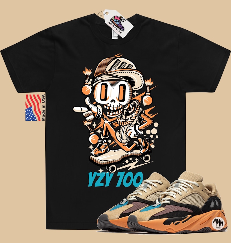 Puede incluir: Camiseta negra con un esqueleto de dibujos animados que lleva un sombrero y patina en monopat&iacute;n. El texto "YZY 100" est&aacute; impreso debajo de la imagen. Un par de zapatillas de deporte de color beige, naranja y azul se muestran debajo de la camiseta.