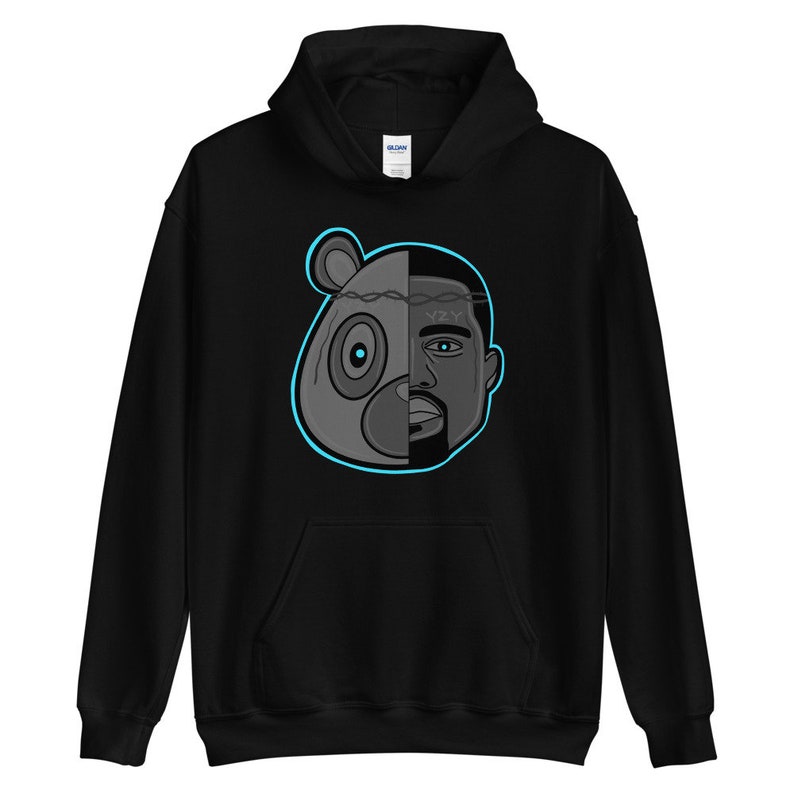 Peut inclure: Sweat-shirt &agrave; capuche noir avec un motif repr&eacute;sentant un ours et le visage de Kanye West, divis&eacute; en deux. L'ours est gris et le visage est noir et blanc. Le motif est soulign&eacute; de bleu.
