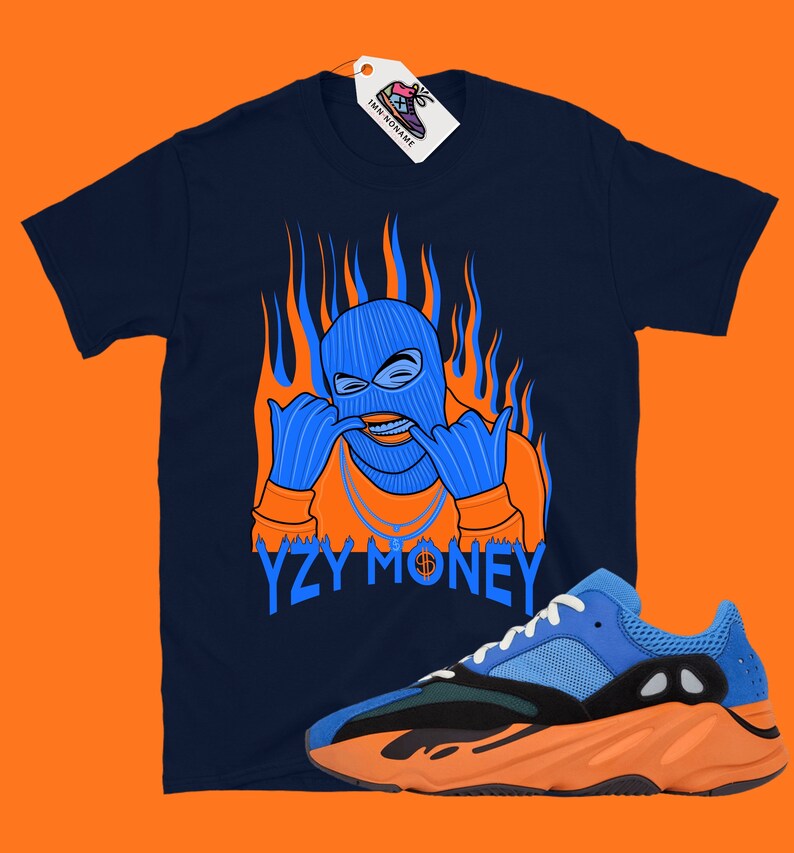 May include: A navy blue t-shirt with an orange and blue illustration of a person wearing a ski mask and a gold chain. The text "YZY MONEY" is printed below the illustration. A pair of blue and orange sneakers are shown in the bottom right corner of the image.
