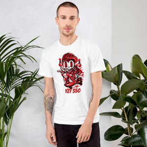 May include: White t-shirt with a red cartoon skeleton skateboarding. The skeleton is wearing a red helmet and holding a red skateboard with the text "VZY 350" on it.