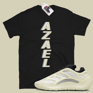 May include: Black t-shirt with the word "AZAEL" printed vertically in a light beige color. A pair of white and beige sneakers with a black tongue and laces.