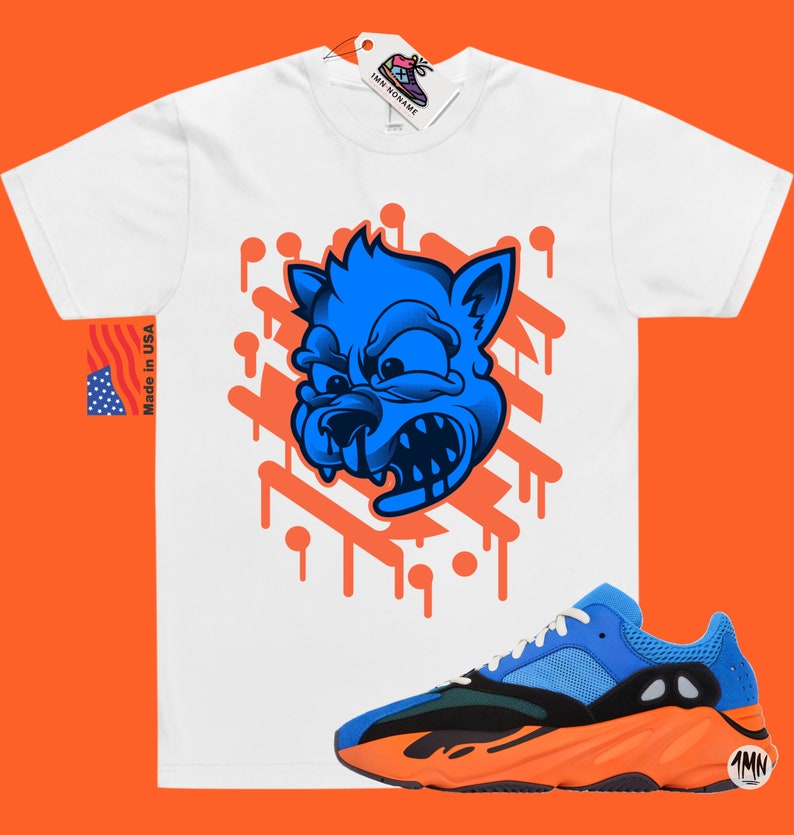 May include: White t-shirt with a blue cartoon wolf graphic and orange paint drips. The t-shirt is paired with orange and blue sneakers with a black swoosh.