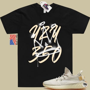 May include: A black t-shirt with a white and tan graphic of a crown with the text "YZY 350" on it. A pair of tan sneakers with a white sole and a tan tag with the text "1MN" on it.