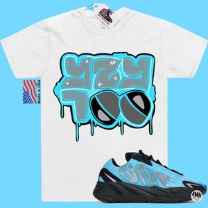 May include: White t-shirt with a blue and gray graphic that says "Yeezy Too" and a pair of blue and black sneakers with the word "Yeezy" on the side.