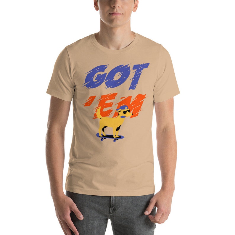 May include: A tan short-sleeved t-shirt with the text "GOT 'EM" in blue, orange, and white. A yellow cartoon dog wearing a blue hat and sunglasses is skateboarding.