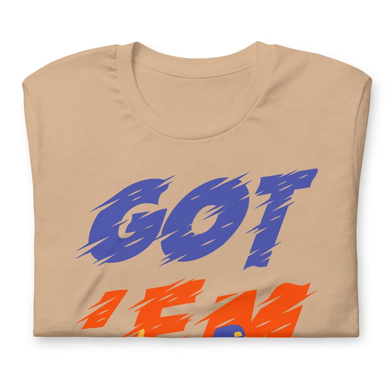 May include: A tan t-shirt with the words "GOT 'EM" printed in blue and orange.