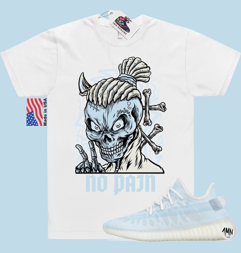 May include: White t-shirt with a graphic of a skull with dreadlocks and the text "no pain". The skull is wearing a necklace with the word "God" on it. The t-shirt is paired with light blue sneakers.