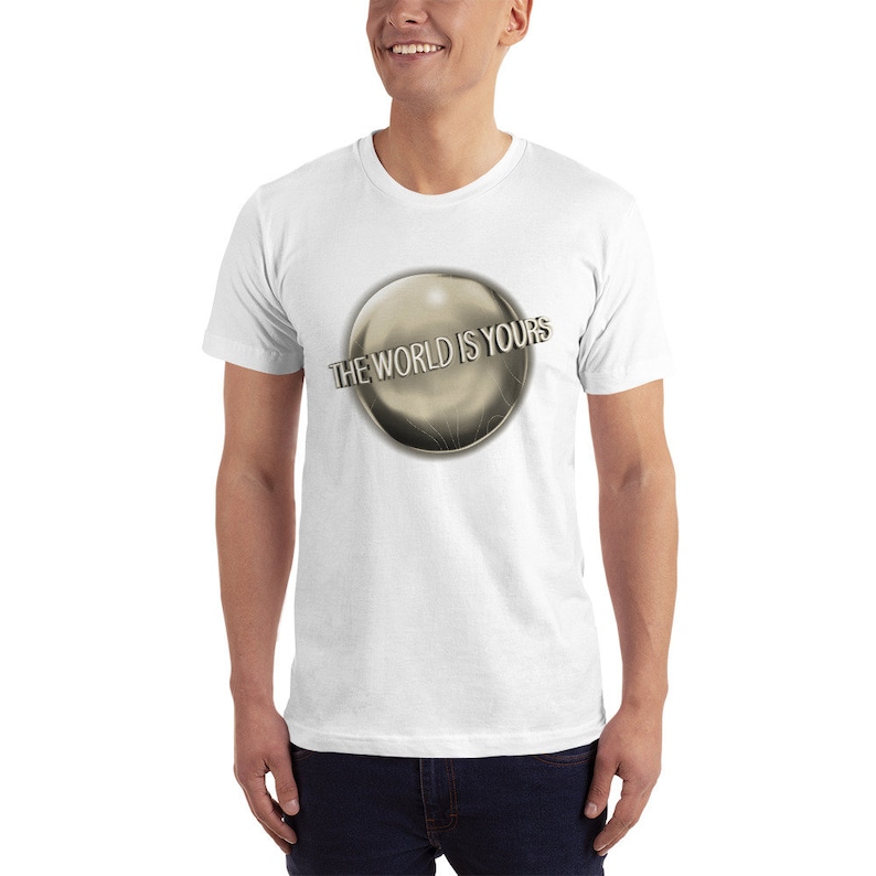 May include: White t-shirt with a silver sphere graphic and the text "THE WORLD IS YOURS" printed on it.
