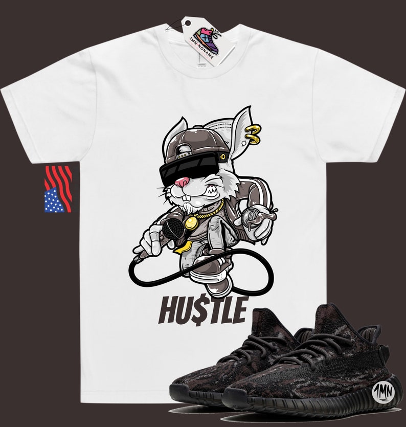 May include: White t-shirt with a cartoon rabbit wearing sunglasses, a gold chain, and a baseball cap. The rabbit is holding a microphone and a spray can. The text "HUSTLE" is printed below the rabbit. A pair of black and grey sneakers with a camouflage pattern are shown below the t-shirt.
