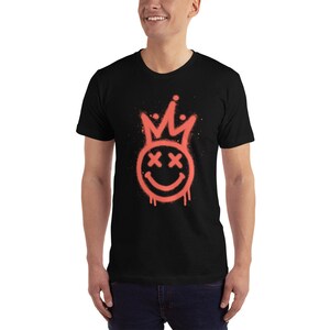 May include: A black t-shirt featuring a red spray paint design of a smiley face with a crown on top. The smiley face has X's for eyes.