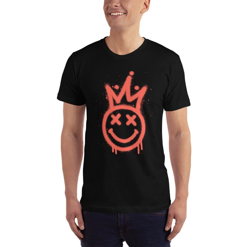May include: A black t-shirt featuring a red spray paint design of a smiley face with a crown on top. The smiley face has X's for eyes.
