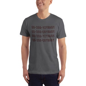 Puede incluir: Una camiseta gris oscuro con el texto "00-350-YZBABY 00-350-CRYBABY 00-350-YZBABY 00-350-CRYBABY" impreso en marr&oacute;n.