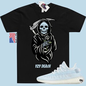 May include: Black t-shirt featuring a graphic of the Grim Reaper holding a flower. The text "YZY DEATH" is printed below the graphic. A pair of white and light blue trainers are shown below the t-shirt.