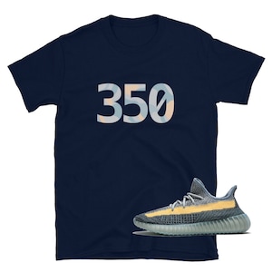 K&ouml;nnte beinhalten: Ein marineblaues T-Shirt mit der Nummer "350" auf der Vorderseite in einem hellblauen und gelben Tarnmuster. Unter dem Shirt ist ein Paar hellblaue und gelbe Sneaker zu sehen.