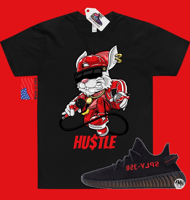 May include: Black t-shirt with a cartoon rabbit wearing a red hat, sunglasses, and a gold chain. The rabbit is holding a microphone and a spray can. The text "HUSTLE" is printed below the rabbit. A pair of black and red sneakers with the text "YZY-350" are shown below the t-shirt.