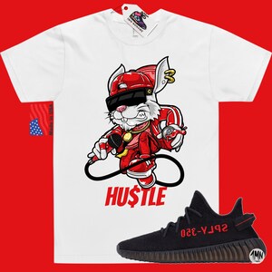 May include: White t-shirt with a cartoon rabbit wearing a red hat, sunglasses, and a gold chain. The rabbit is holding a microphone and spray paint can. The text "HUSTLE" is printed below the rabbit. Black and red sneakers with the text "YZY-350" are shown below the t-shirt.