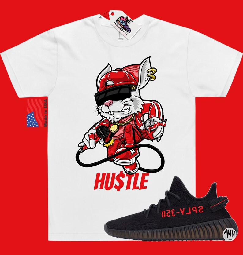 May include: White t-shirt with a cartoon rabbit wearing a red hat, sunglasses, and a gold chain. The rabbit is holding a microphone and spray paint can. The text "HUSTLE" is printed below the rabbit. Black and red sneakers with the text "YZY-350" are shown below the t-shirt.