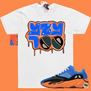 May include: White t-shirt with a blue and orange graphic that says "#YZY 700" with a pair of sunglasses.  The t-shirt is paired with orange and blue sneakers.