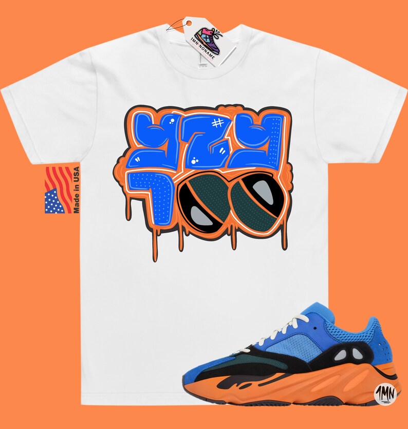 May include: White t-shirt with a blue and orange graphic that says "#YZY 700" with a pair of sunglasses.  The t-shirt is paired with orange and blue sneakers.