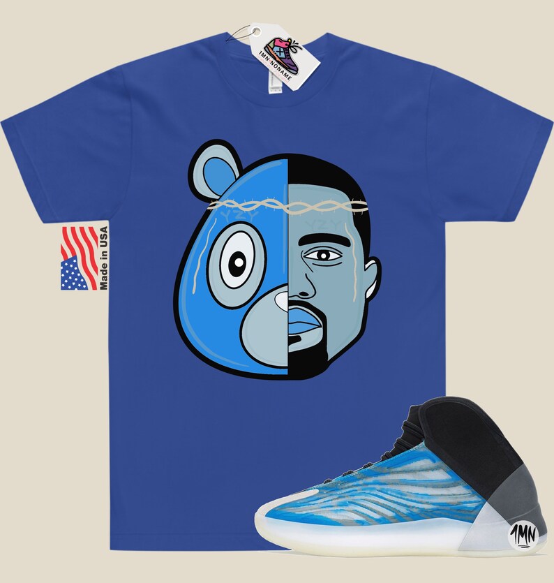 May include: A blue t-shirt with a graphic of a blue bear and Kanye West's face. The graphic has a barbed wire crown on top. The t-shirt is paired with a blue and white sneaker with a black upper and a white sole. The sneaker has a black tag with the letters "1MN" on it.