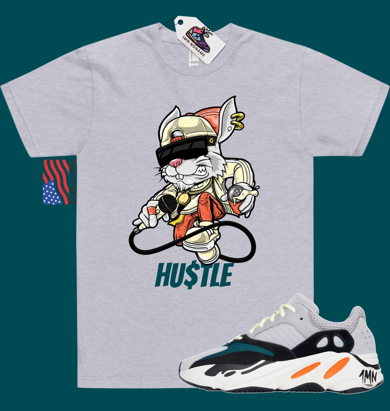 May include: A grey t-shirt featuring a cartoon rabbit wearing sunglasses, a hat, and a gold chain. The rabbit is holding a microphone and a spray can. The text "HUSTLE" is printed below the rabbit. A pair of white, green, and orange trainers are shown below the t-shirt.