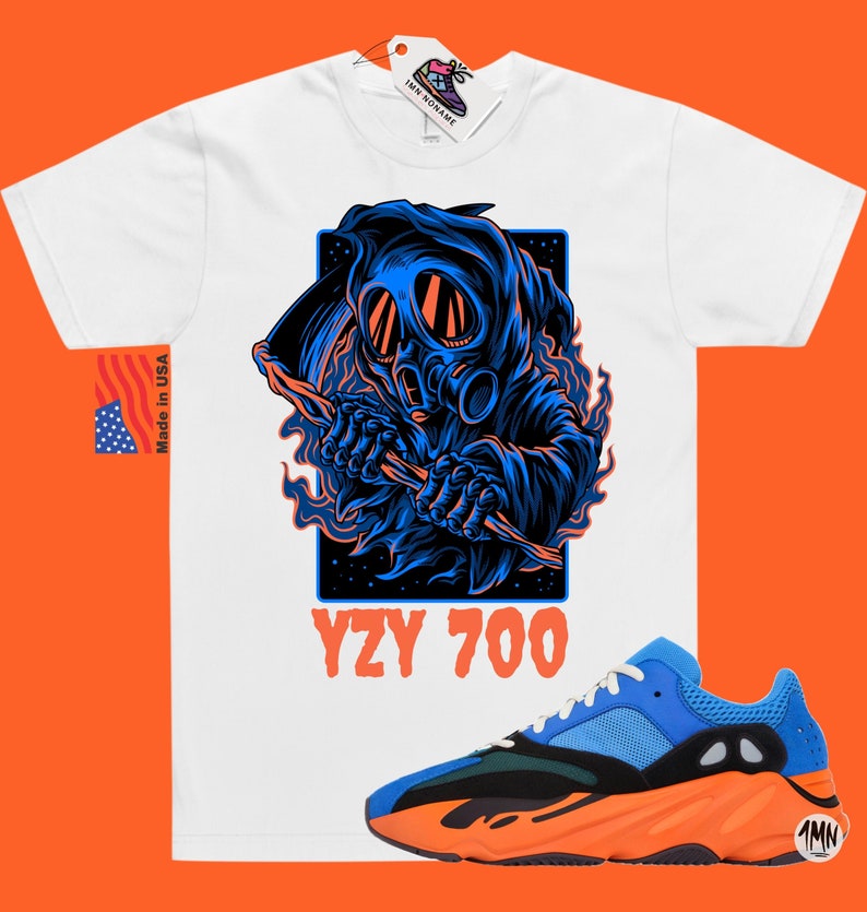 May include: White t-shirt with a blue and black graphic of a hooded figure wearing a gas mask and holding a scythe. The text "YZY 700" is printed below the graphic. A pair of blue and orange sneakers with the text "1MN" on the side are shown below the t-shirt.