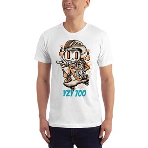 Puede incluir: Camiseta blanca con una ilustraci&oacute;n de dibujos animados de un esqueleto haciendo skateboard. El esqueleto lleva un sombrero, gafas de sol y un pa&ntilde;uelo. El texto "YZY 700" est&aacute; impreso debajo de la ilustraci&oacute;n.