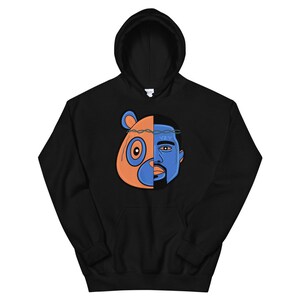 May include: Black hoodie with a graphic of a bear and a person's face. The bear is orange and the person's face is blue. The graphic is split down the middle, with the bear on the left and the person on the right. The person has a crown of thorns on their head. The text "YZY" is visible on the person's forehead.