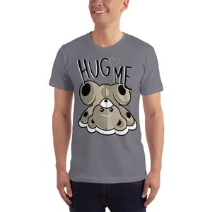 Puede incluir: Una camiseta gris jaspeada con un osito de peluche de dibujos animados que lleva un coraz&oacute;n en el pecho y el texto "HUG ME" encima.