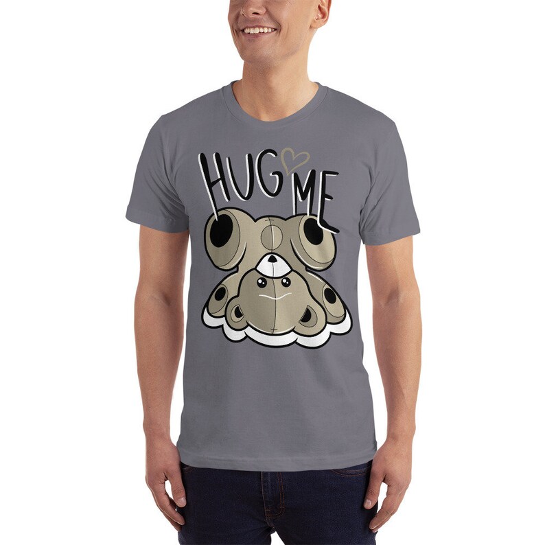 Puede incluir: Una camiseta gris jaspeada con un osito de peluche de dibujos animados que lleva un coraz&oacute;n en el pecho y el texto "HUG ME" encima.