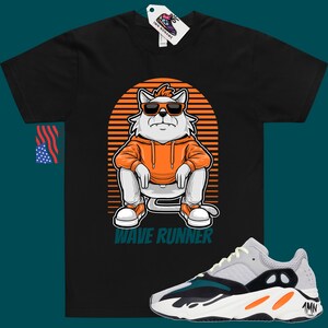 May include: Black t-shirt with a cartoon cat wearing sunglasses and an orange hoodie. The cat is sitting on a striped background with the text "Wave Runner". A pair of white, grey, green, and orange sneakers are shown below the t-shirt.