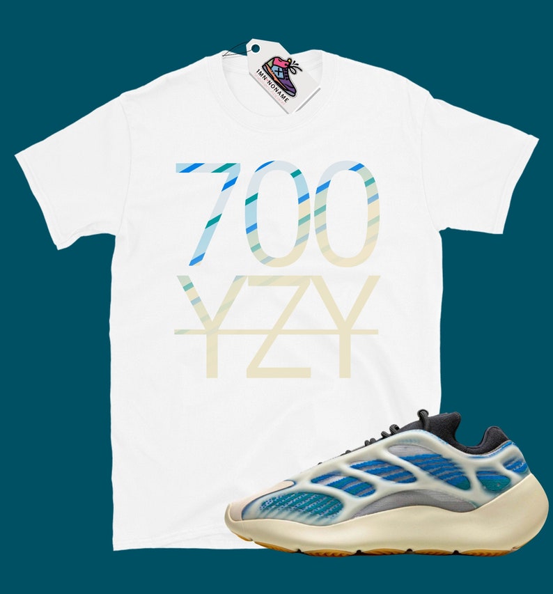 Puede incluir: Camiseta blanca con "700 YZY" impreso en rayas azules y verdes. Un par de zapatillas blancas y azules con suela negra.