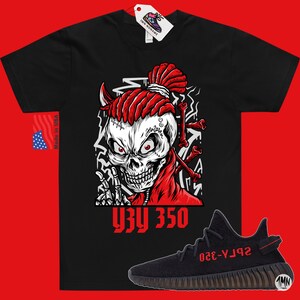 Op de afbeelding: Zwart T-shirt met een rode schedelprint en de tekst "YZY 350". Onder het T-shirt is een paar zwarte en rode Yeezy 350 sneakers te zien.