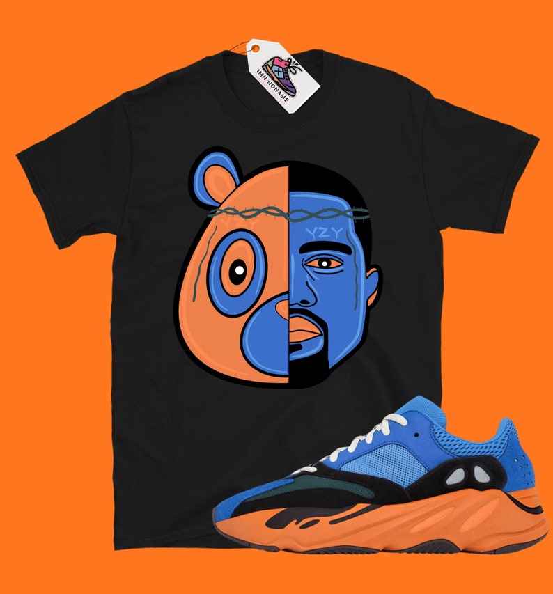 Pode incluir: Camiseta preta com um gr&aacute;fico de um urso de desenho animado e o rosto de Kanye West. O gr&aacute;fico &eacute; dividido em dois, com o urso &agrave; esquerda e Kanye &agrave; direita. O urso est&aacute; usando uma coroa de espinhos. A camiseta &eacute; combinada com t&ecirc;nis Yeezy laranja e azul.