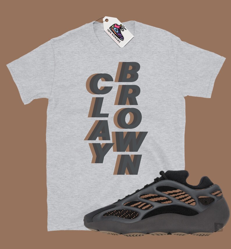 May include: A light gray t-shirt with the word "CBRLOAWYN" in a layered, shadow effect design. A black and brown athletic shoe is positioned below the shirt. A tag with a shoe graphic hangs from the shirt.