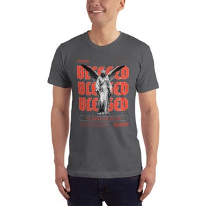 May include: A dark gray t-shirt with a graphic print of a winged angel statue. The text "Blessed" is repeated three times in red, and the text "Guardian of Death" is printed below the image.