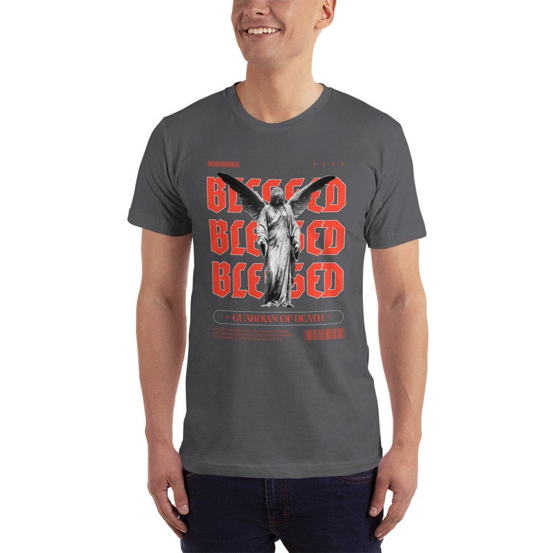 May include: A dark gray t-shirt with a graphic print of a winged angel statue. The text "Blessed" is repeated three times in red, and the text "Guardian of Death" is printed below the image.
