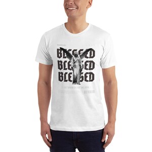 May include: White t-shirt with a black and white graphic print of an angel with wings and the text "Blessed" repeated four times. The text "Guardian of Death" is also printed on the shirt.