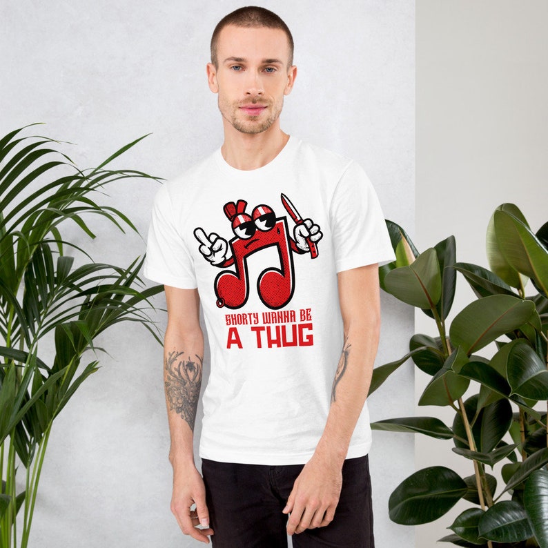 Puede incluir: Camiseta blanca con una nota musical roja de dibujos animados que sostiene un cuchillo y el texto "Shorty Wanna Be A Thug".