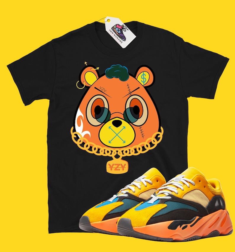 May include: Black t-shirt featuring an orange bear graphic with gold chain, glasses, and dollar sign. Paired with orange, yellow, and blue sneakers. The tag reads "IMN NONAME".