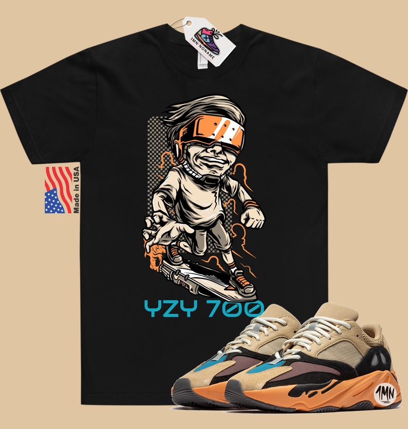 May include: Black t-shirt with a cartoon illustration of a person wearing a futuristic helmet and riding a skateboard. The text "YZY 700" is printed below the illustration. A pair of tan, orange, and blue sneakers are shown below the t-shirt.