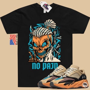 May include: Black t-shirt with a cartoon skull graphic and the text "no pain".  The skull has blue eyes, a blue and orange bandana, and a dreadlock hairstyle.  A pair of tan, orange, and blue sneakers are shown below the t-shirt.