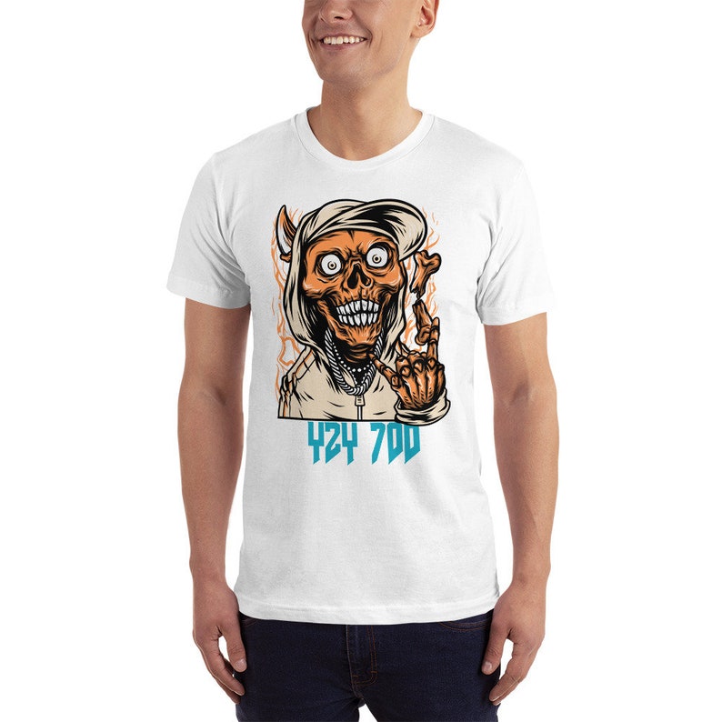 May include: White t-shirt with a graphic of a cartoon skull wearing a hoodie and a backwards hat. The skull is making a hand gesture and the text "424 700" is printed below the skull.