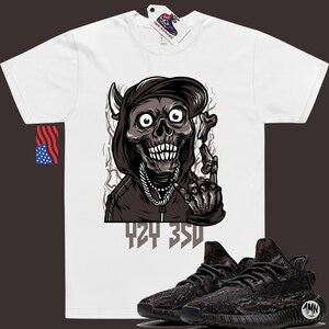 Puede incluir: Camiseta blanca con un gr&aacute;fico de una calavera con capucha y una cadena, con el texto "424 350" debajo. Tambi&eacute;n se muestra un par de zapatillas de deporte de camuflaje negro y marr&oacute;n.