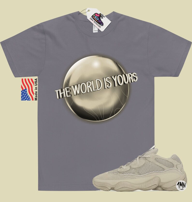 May include: A gray t-shirt with the text "The World Is Yours" printed on a gold sphere. A pair of beige sneakers with a mesh upper and a thick sole are shown below the t-shirt.