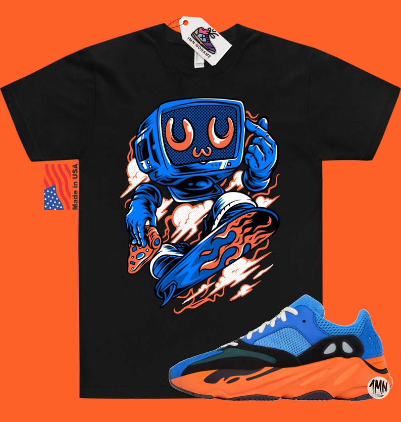 May include: Black t-shirt with a cartoon illustration of a blue robot holding a video game controller and riding a flaming skateboard. The robot has a blue television screen for a head with a cartoon face. The t-shirt is paired with a pair of orange and blue sneakers with the text "1MN" on the side.