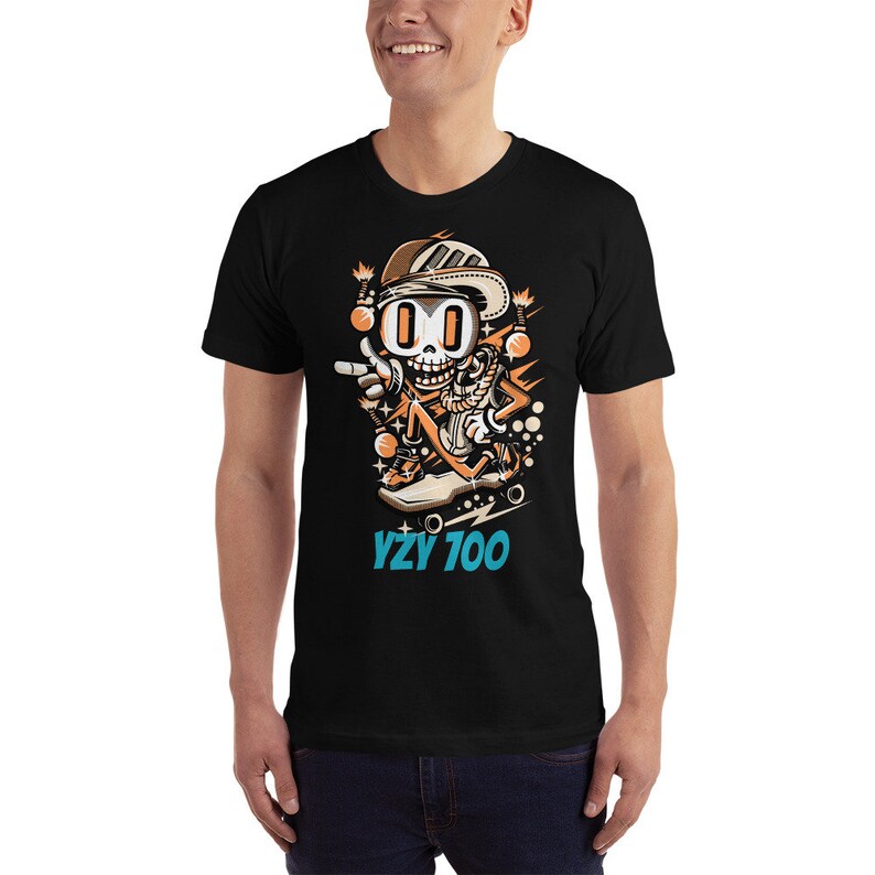 Puede incluir: Camiseta negra con una ilustraci&oacute;n de dibujos animados de un esqueleto con un sombrero y montando un monopat&iacute;n. El texto "YZY 700" est&aacute; impreso debajo de la ilustraci&oacute;n.