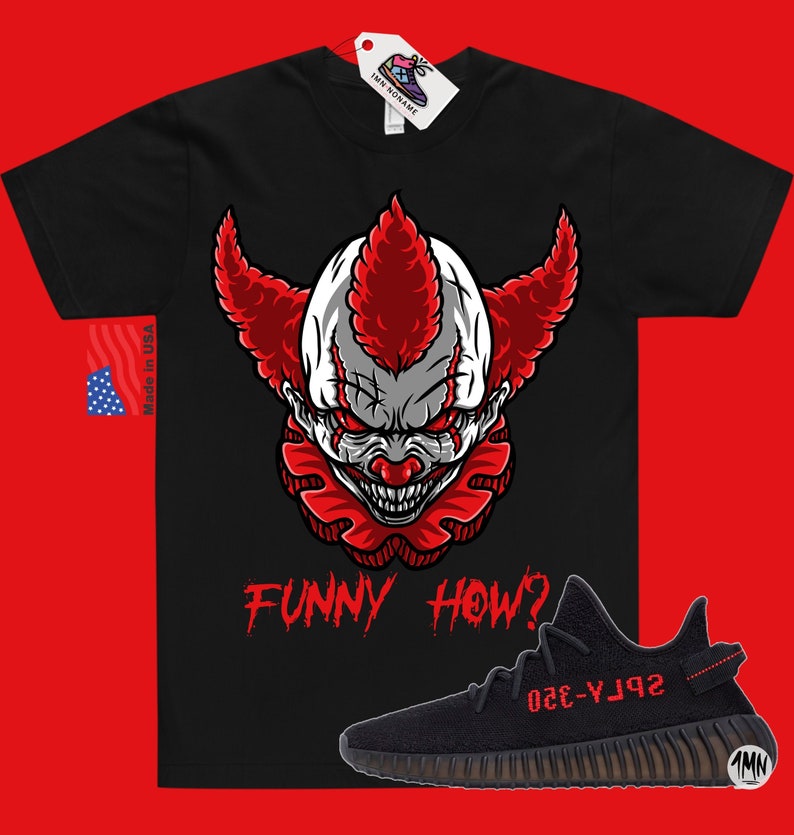 May include: Black t-shirt with a red and white clown face graphic and the text "FUNNY HOW?" in red. A black and red Yeezy 350 Boost sneaker is shown below the shirt.