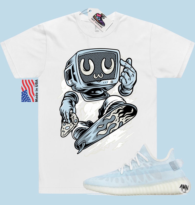 May include: White t-shirt with a cartoon illustration of a robot with a television for a head, riding a snowboard. The robot is wearing a blue and white spacesuit and has a blue and white snowboard with flames on the bottom. The t-shirt has the text "Made in USA" on the left side. The image also includes a pair of white and light blue sneakers with the text "1MN" on the side.